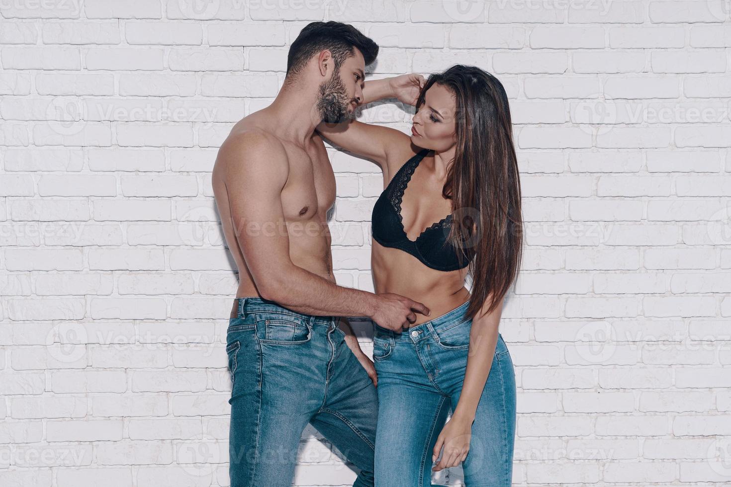Beautiful young couple looking at each other while standing against brick wall photo