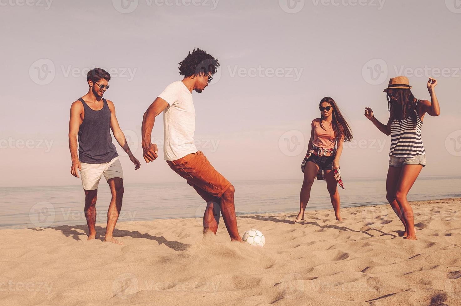 Beach ball. Group of cheerful young people playing with soccer ball on the beach with sea in the background photo