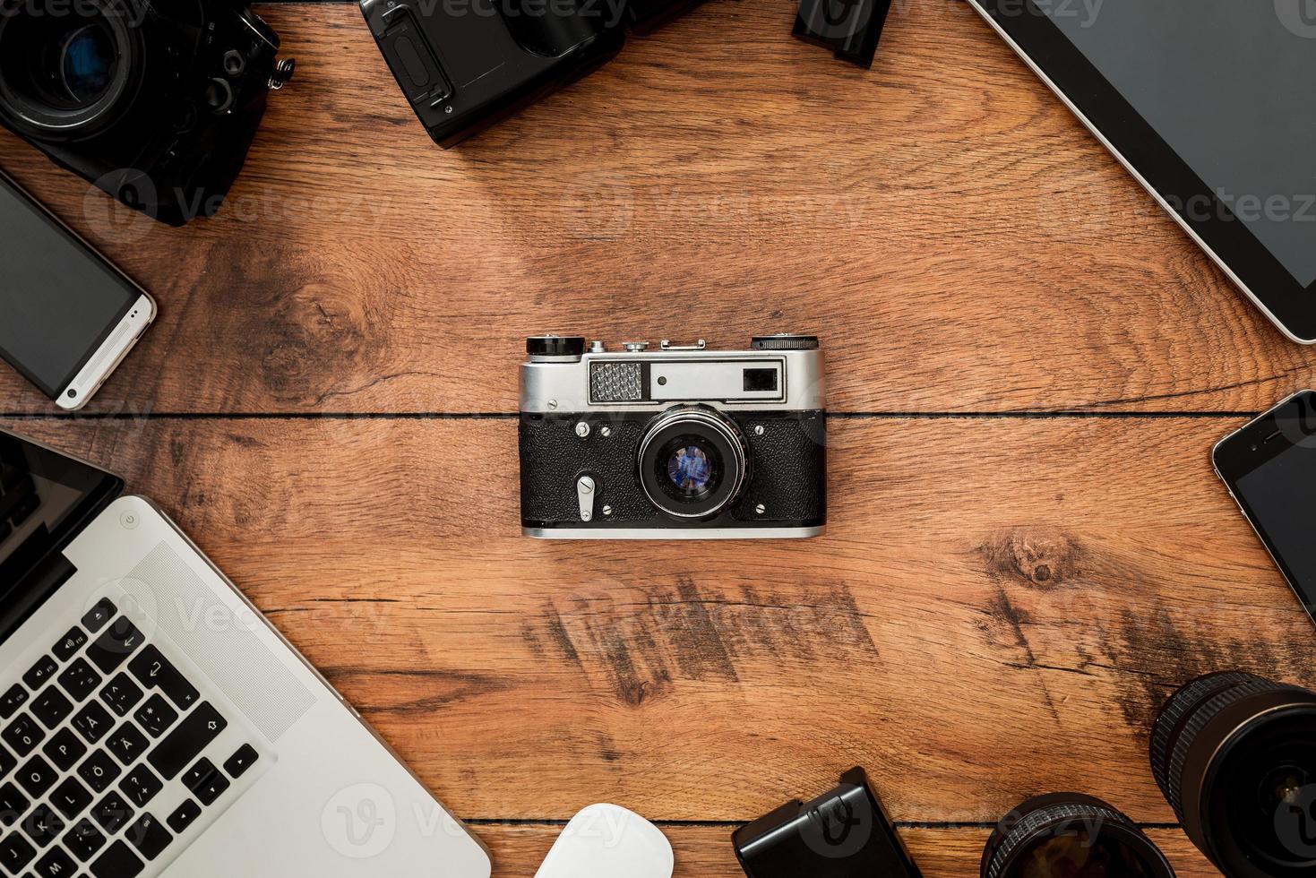 Displacement of old technology. Top view of retro camera surrounding by diverse equipment for photographer laying on the wooden grain photo