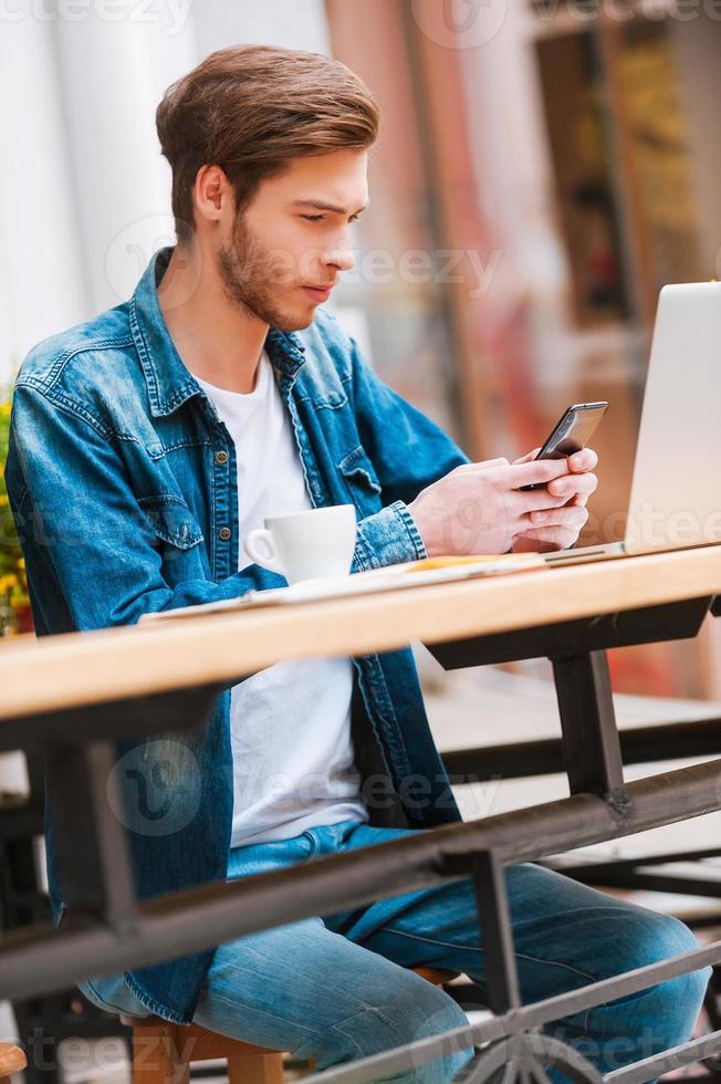 Sending urgent message. Concentrated young man holding mobile phone while sitting at sidewalk cafe photo