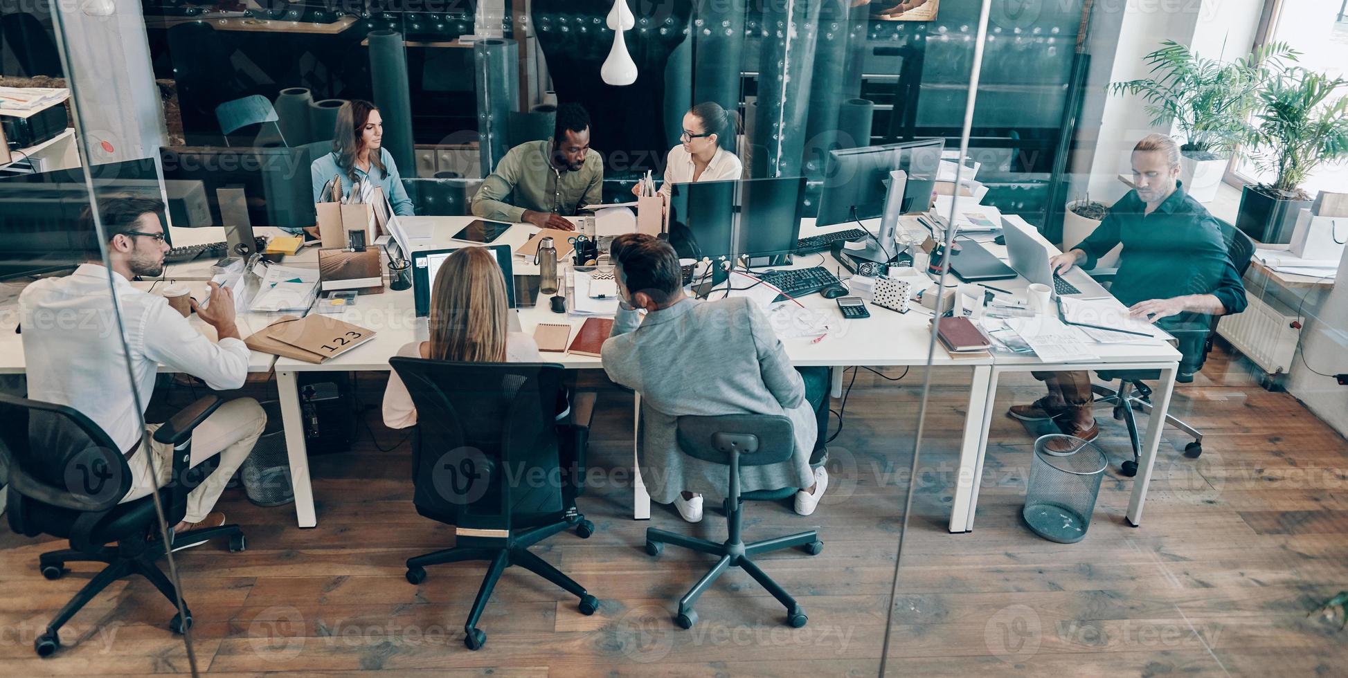 Top view of young modern people in smart casual wear communicating and using modern technologies while working in the office photo