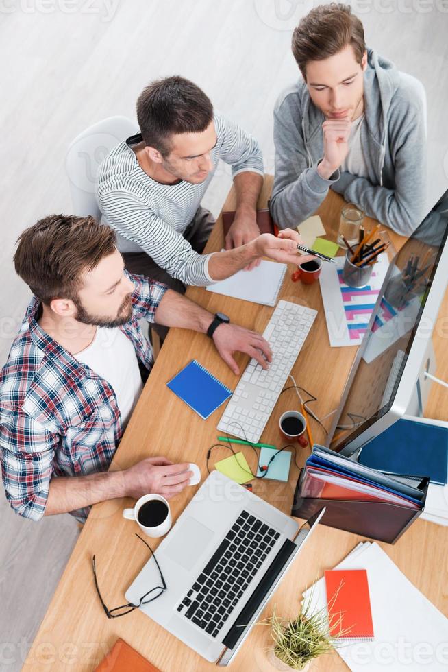 Working on a new project. Top view of concentrated three young men working together while sitting at working place photo