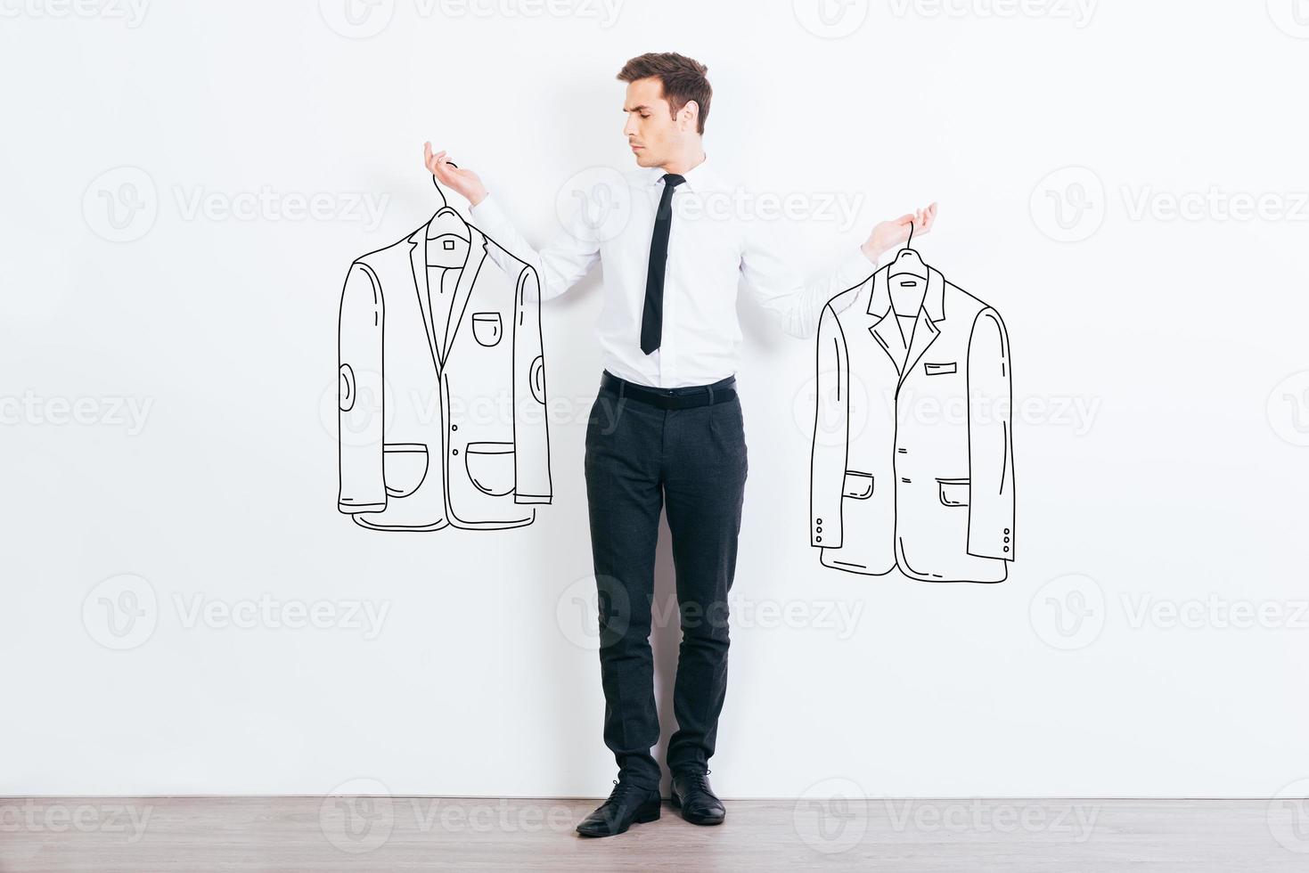 What jacket shall I choose  Handsome young man choosing between two drawn jackets while standing against white background photo