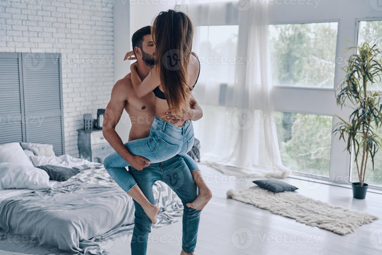 Handsome young shirtless man carrying semi-dressed attractive woman while standing in the bedroom photo