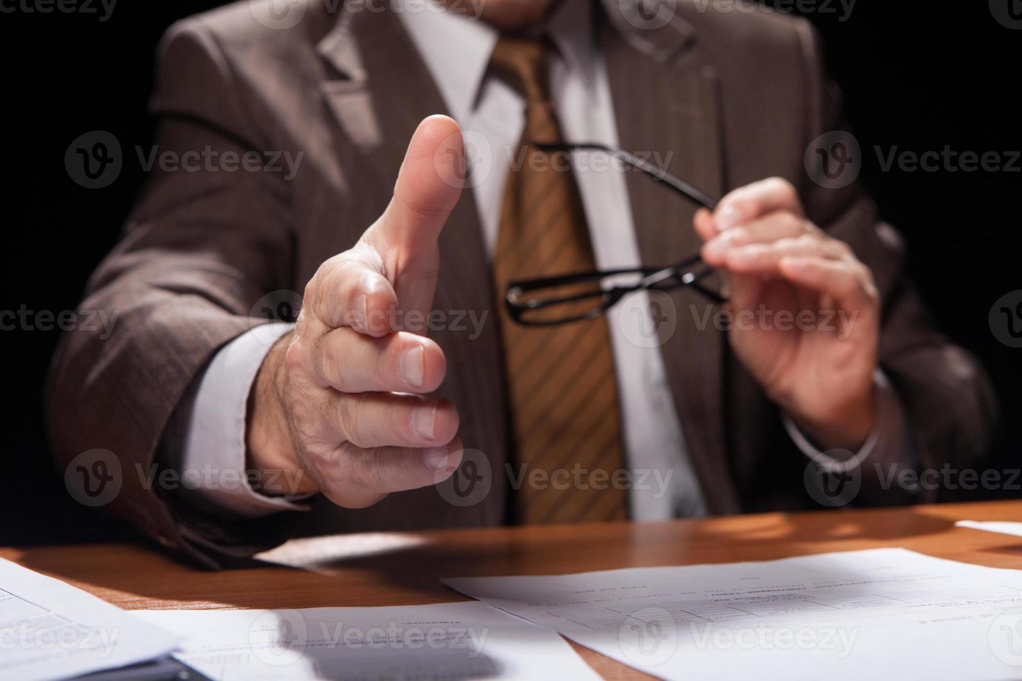 Welcome on board. Cropped image of man in formalwear sitting at his working place and stretching out his hand for shaking while isolated on black background photo
