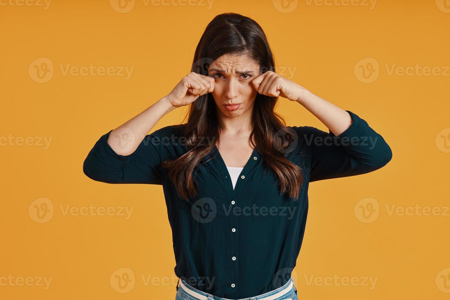 Sad young woman in casual clothing making a face while standing against yellow background photo