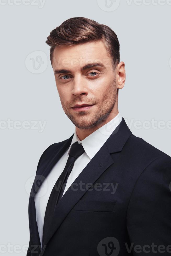 Always in style. Handsome young man in full suit looking at camera with smile while standing against grey background photo
