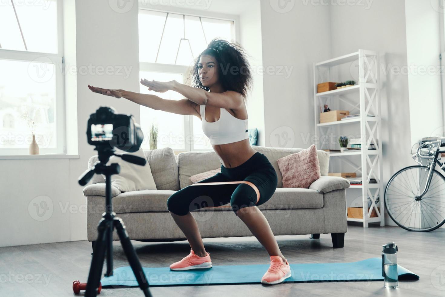 hermosa joven africana agachada usando una correa mientras hace un video en las redes sociales foto