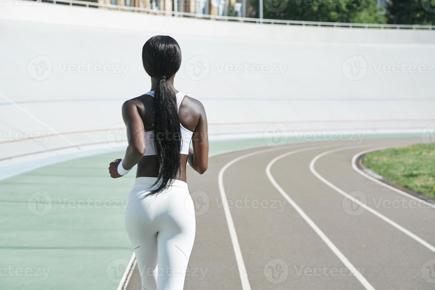 Rear view of beautiful young African woman in sports clothing running on track outdoors photo