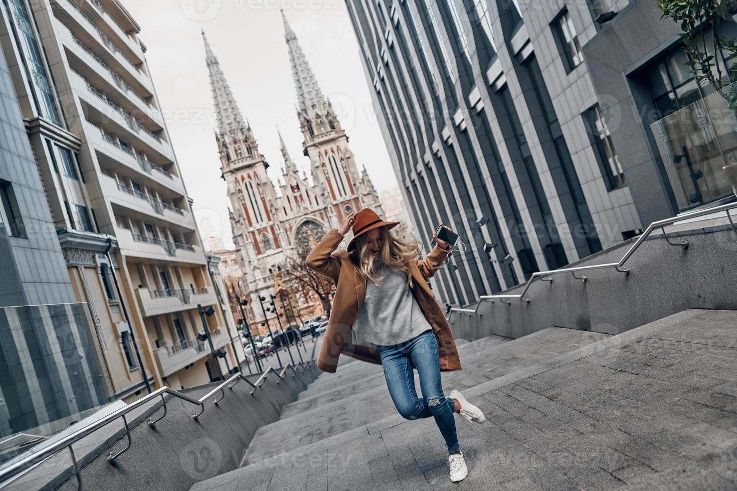 Young and full of energy. Full length of attractive young woman listening music and dancing while spending carefree time in the city photo