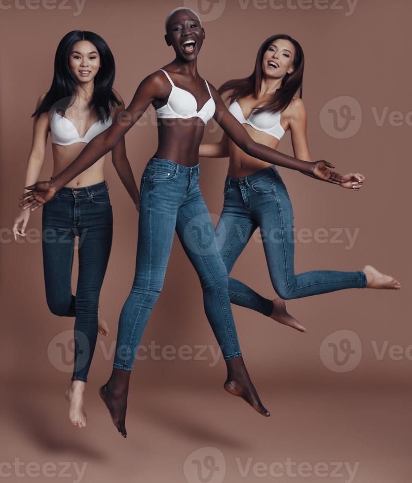 So much fun Full length of three attractive young women looking at camera and smiling while jumping against brown background photo