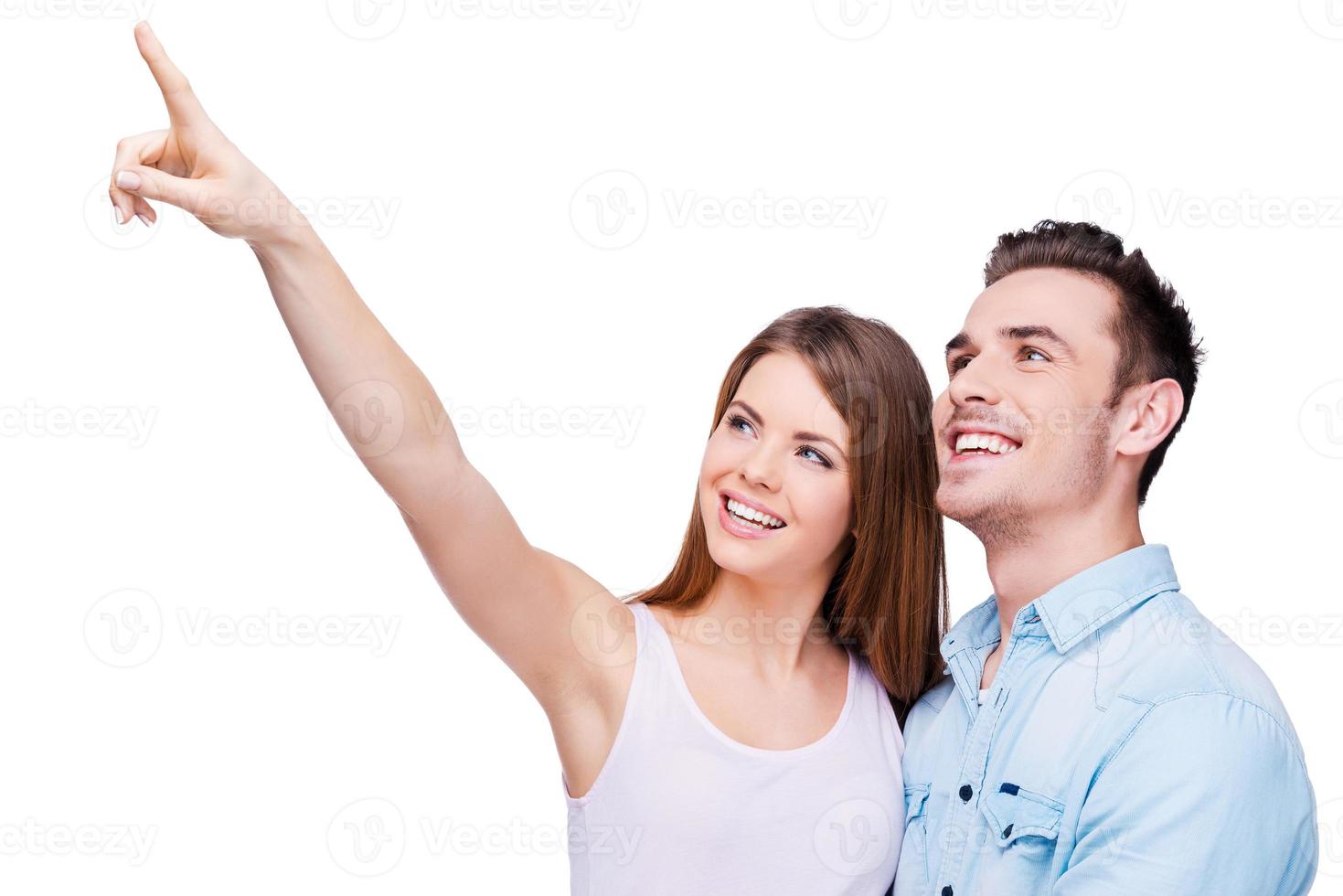 Look over there Happy young loving couple bonding to each other while beautiful woman pointing away and smiling photo