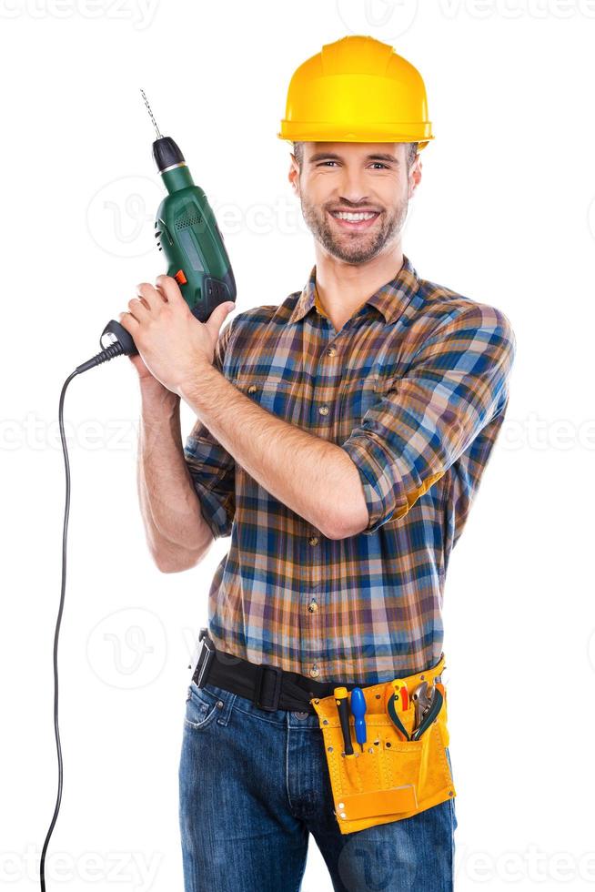 Always ready to help. Confident young male carpenter in hardhat holding drill and looking at camera with smile while standing against white background photo