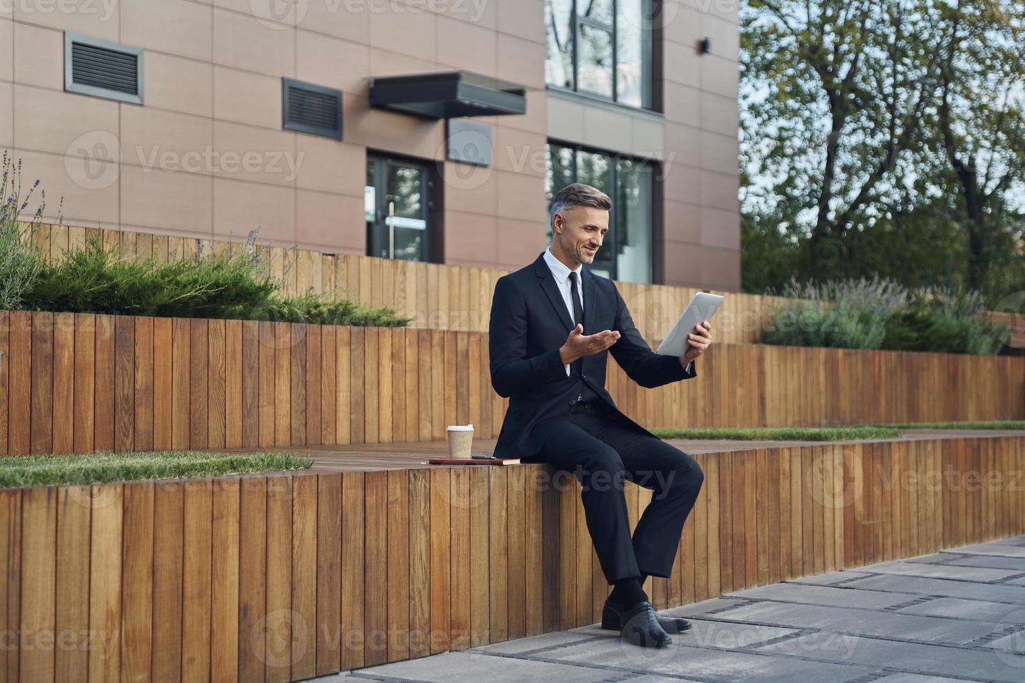 Confident mature businessman using digital tablet while sitting outdoors near office building photo