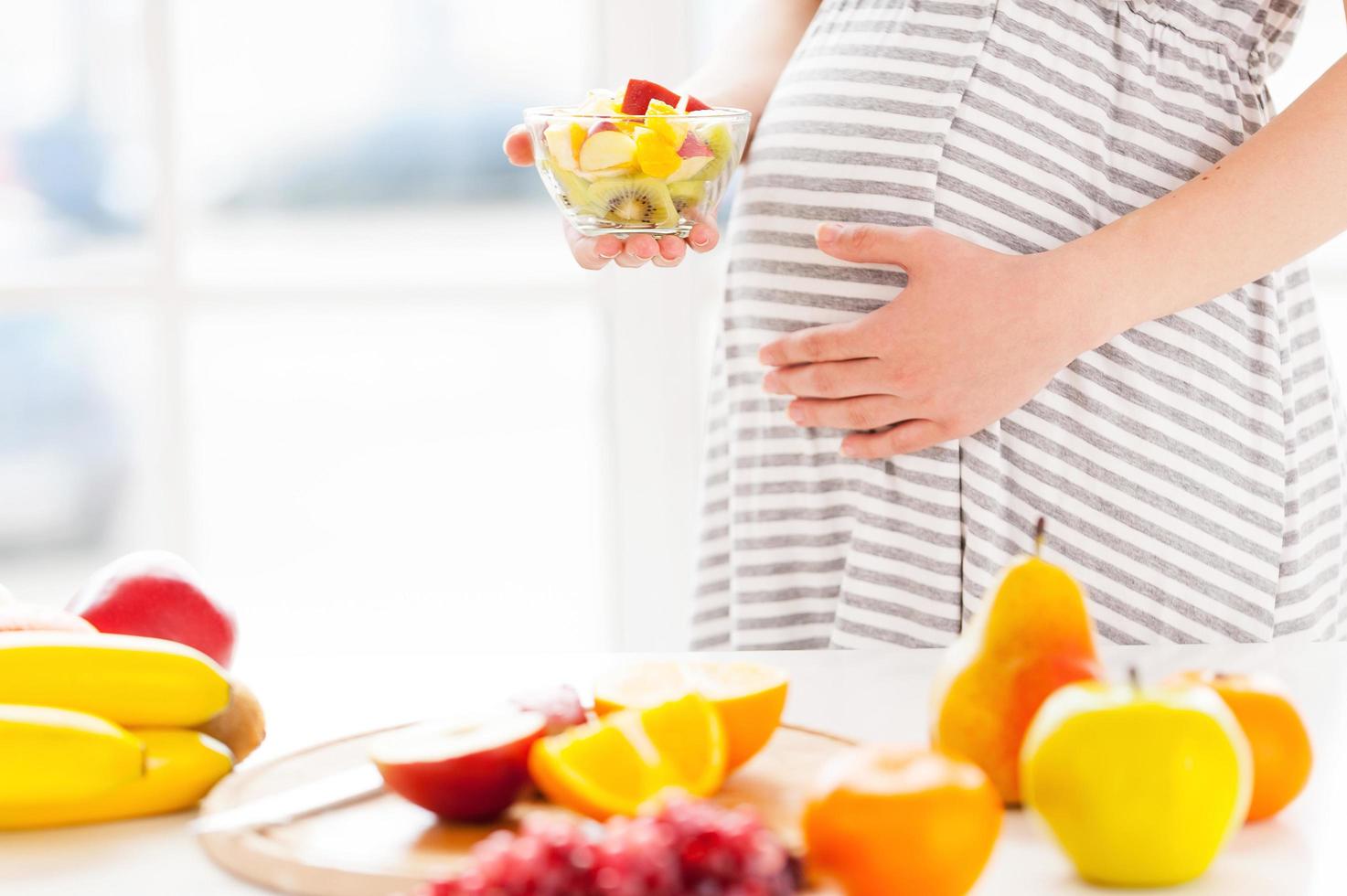 solo comida fresca y sana para mi bebe. imagen recortada de una mujer embarazada sosteniendo un plato con ensalada de frutas foto