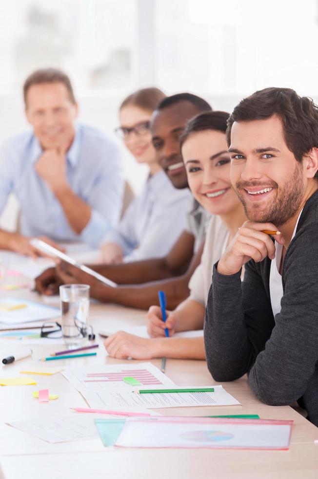 Business meeting. Group of business people in casual wear sitting in a row at the table and smiling at camera photo