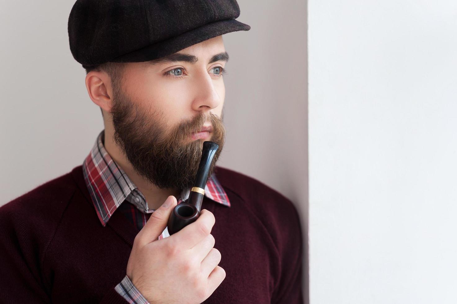 fumando una pipa. retrato de un apuesto joven con sombrero fumando una pipa y mirando hacia otro lado foto