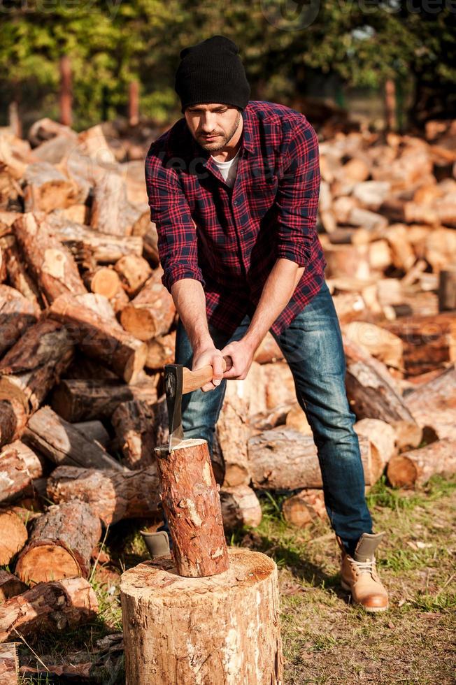 Skilled forester. Full length of confident young forester cutting log while standing outdoors photo