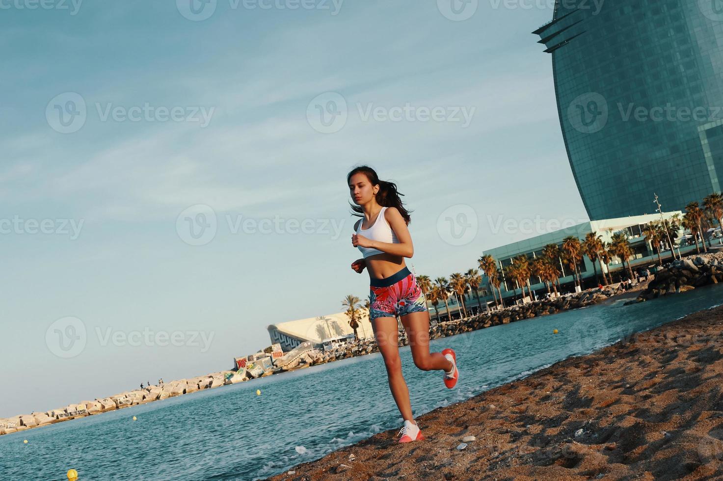 llena de energía. toda la longitud de una joven atractiva con ropa deportiva trotando mientras hace ejercicio al aire libre foto