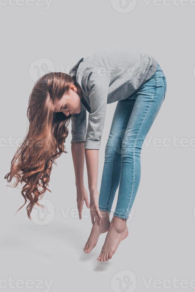 Mid-air beauty. Mid-air shot of attractive young woman in casual wear bending in front of grey background photo