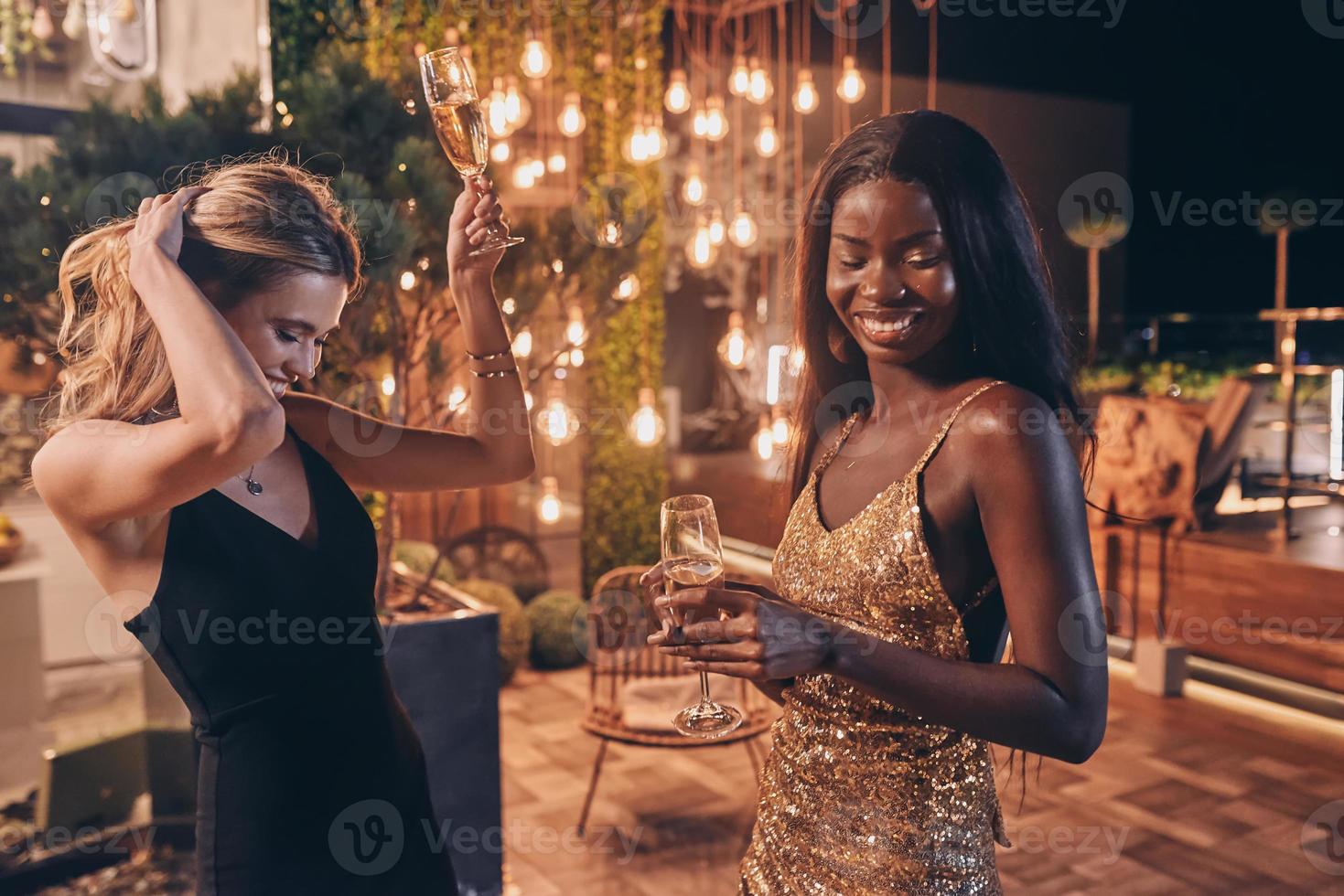 Two beautiful women in evening gowns dancing and smiling while spending time on luxury party photo