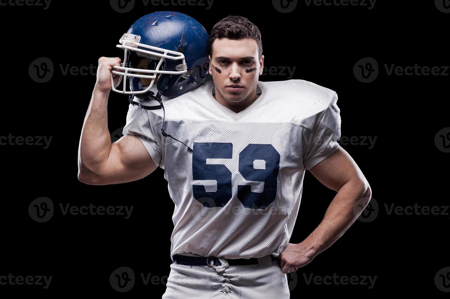 He is ready to win  American football player looking at camera and carrying helmet on his shoulder while standing against black background photo