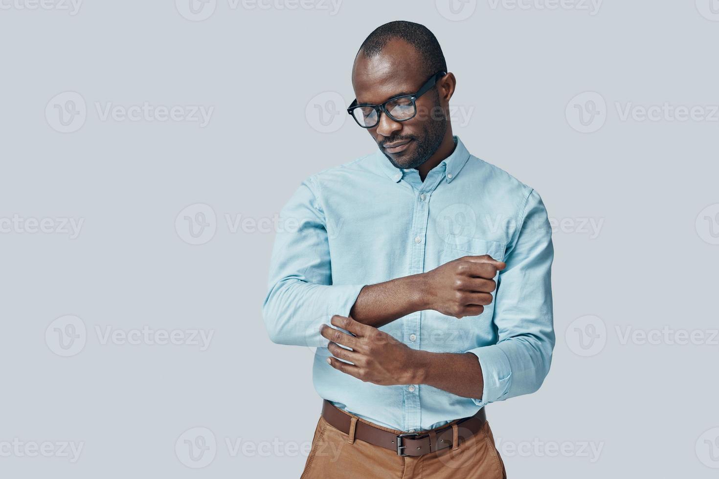 Fashionable young African man adjusting sleeve while standing against grey background photo