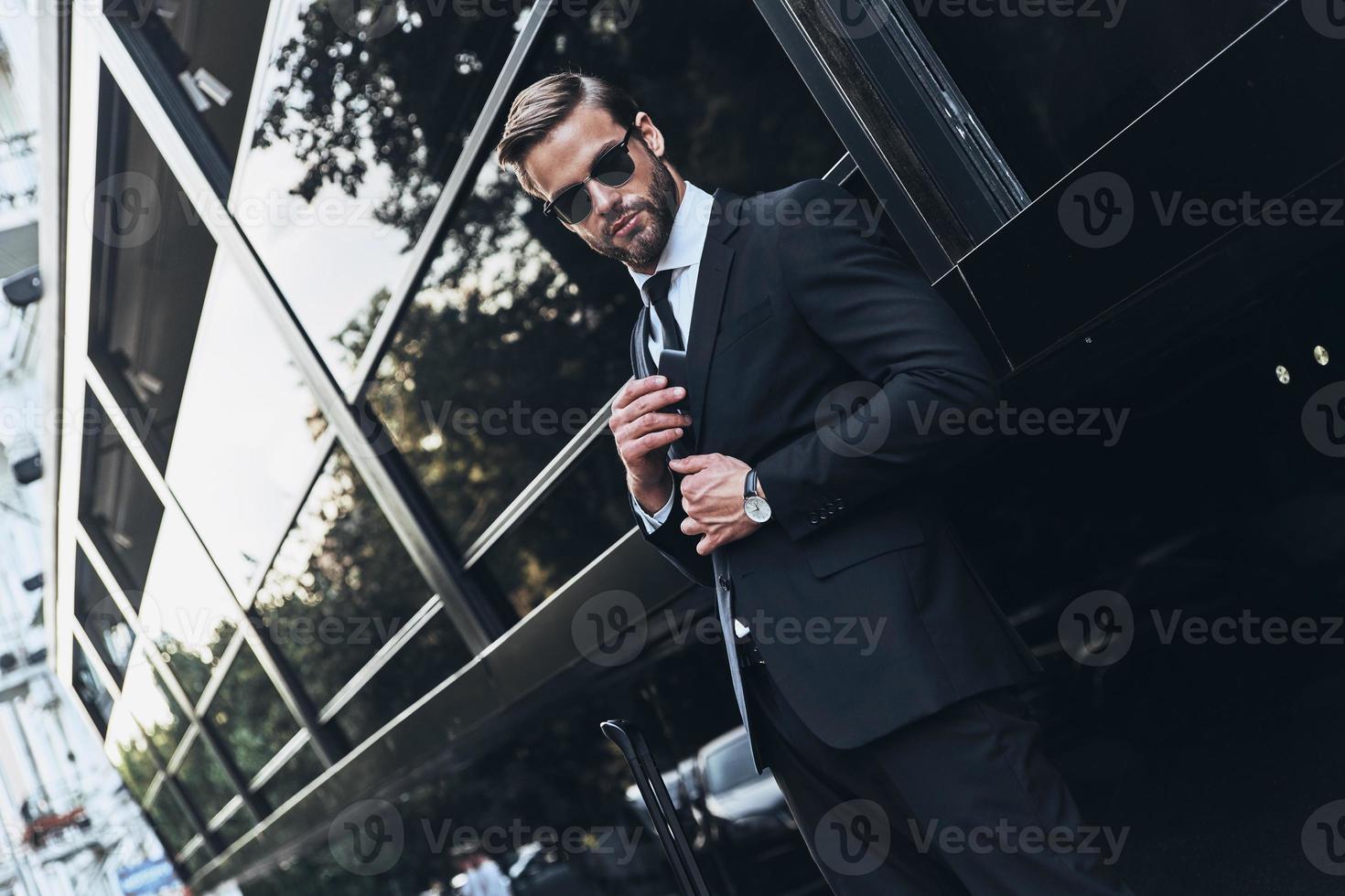 Young and successful. Handsome young man in full suit adjusting his jacket while standing outdoors photo