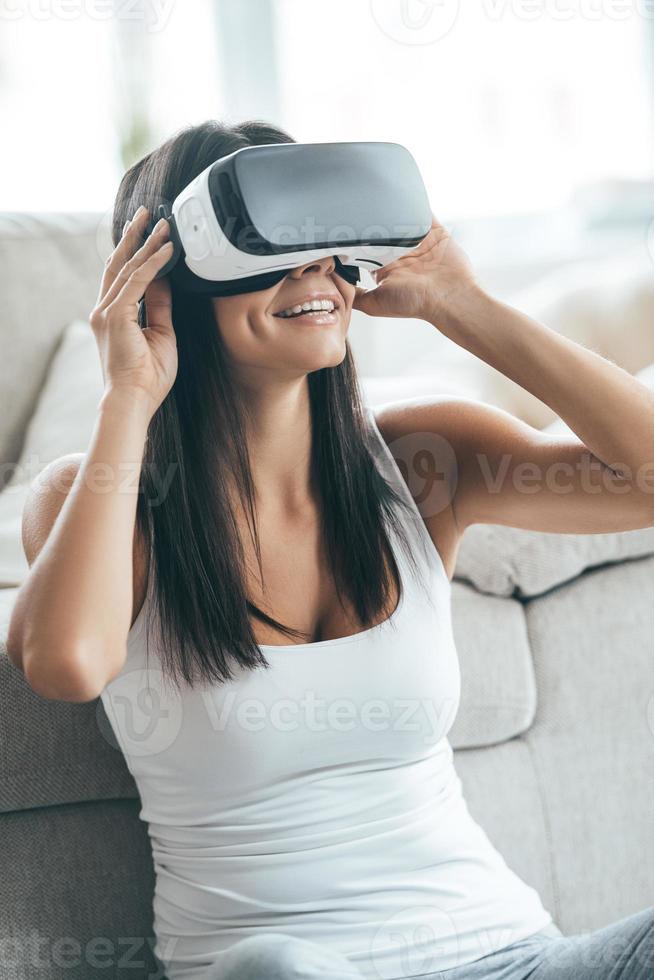 Future is now. Attractive young woman adjusting her VR headset and smiling while sitting at home photo