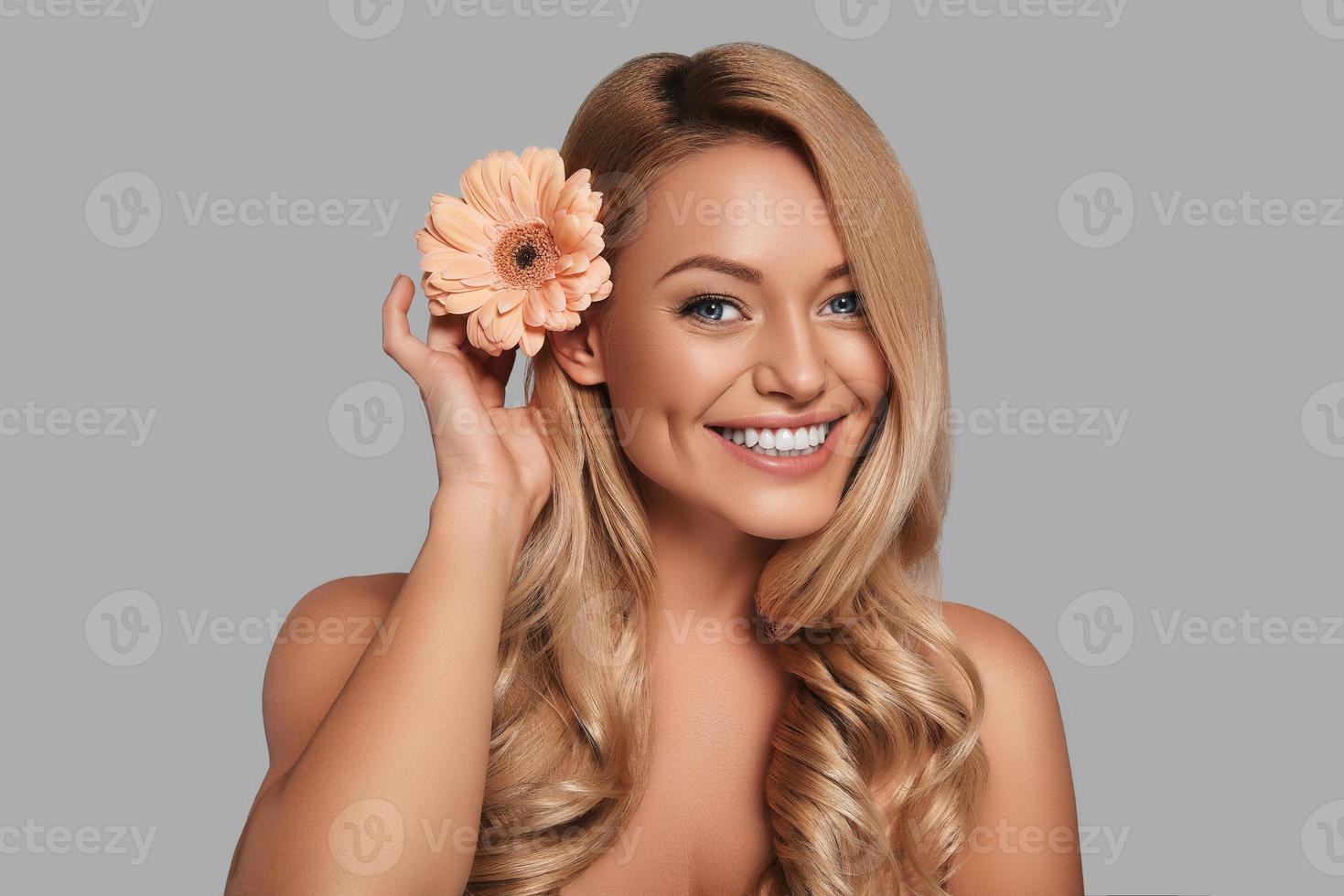 Playful young woman looking at camera and smiling while standing against grey background photo