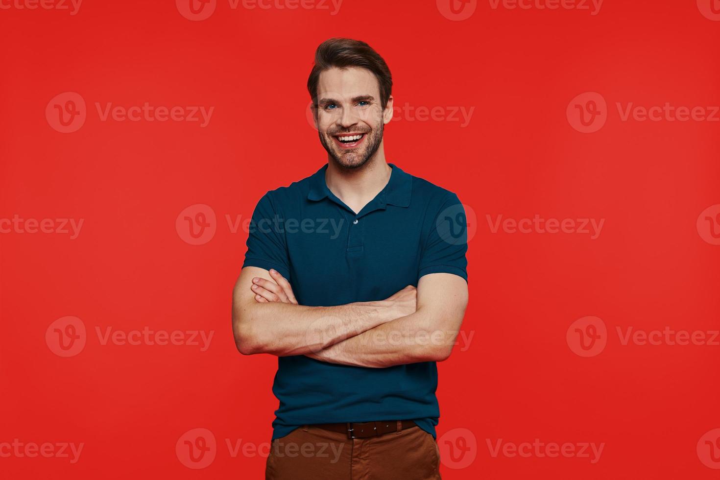 Cheerful young man in casual wear looking at camera and keeping arms crossed photo