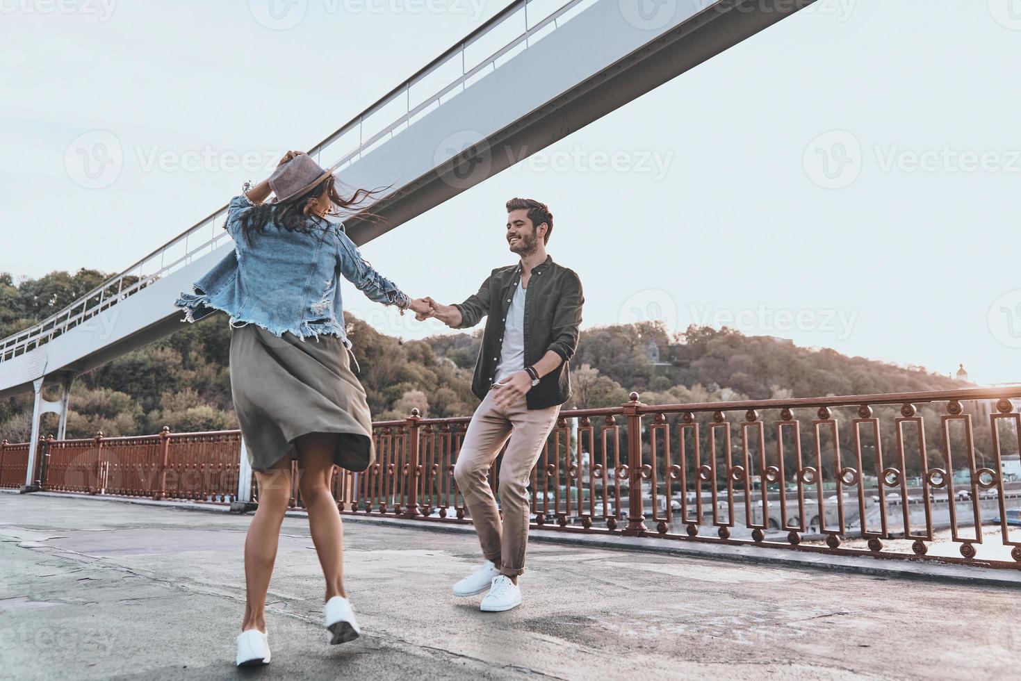 Love is in the air. Full length of playful young couple holding hands and spinning while dancing on the bridge outdoors photo