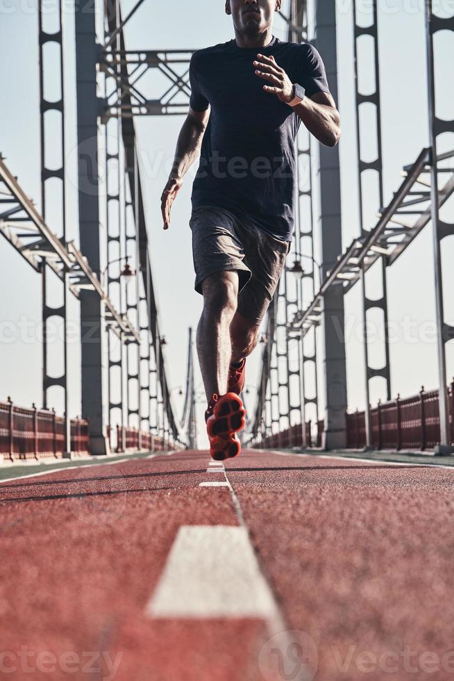 entrenamiento de la mañana. Cerca de un joven africano vestido con ropa deportiva haciendo ejercicio mientras trotaba en el puente al aire libre foto