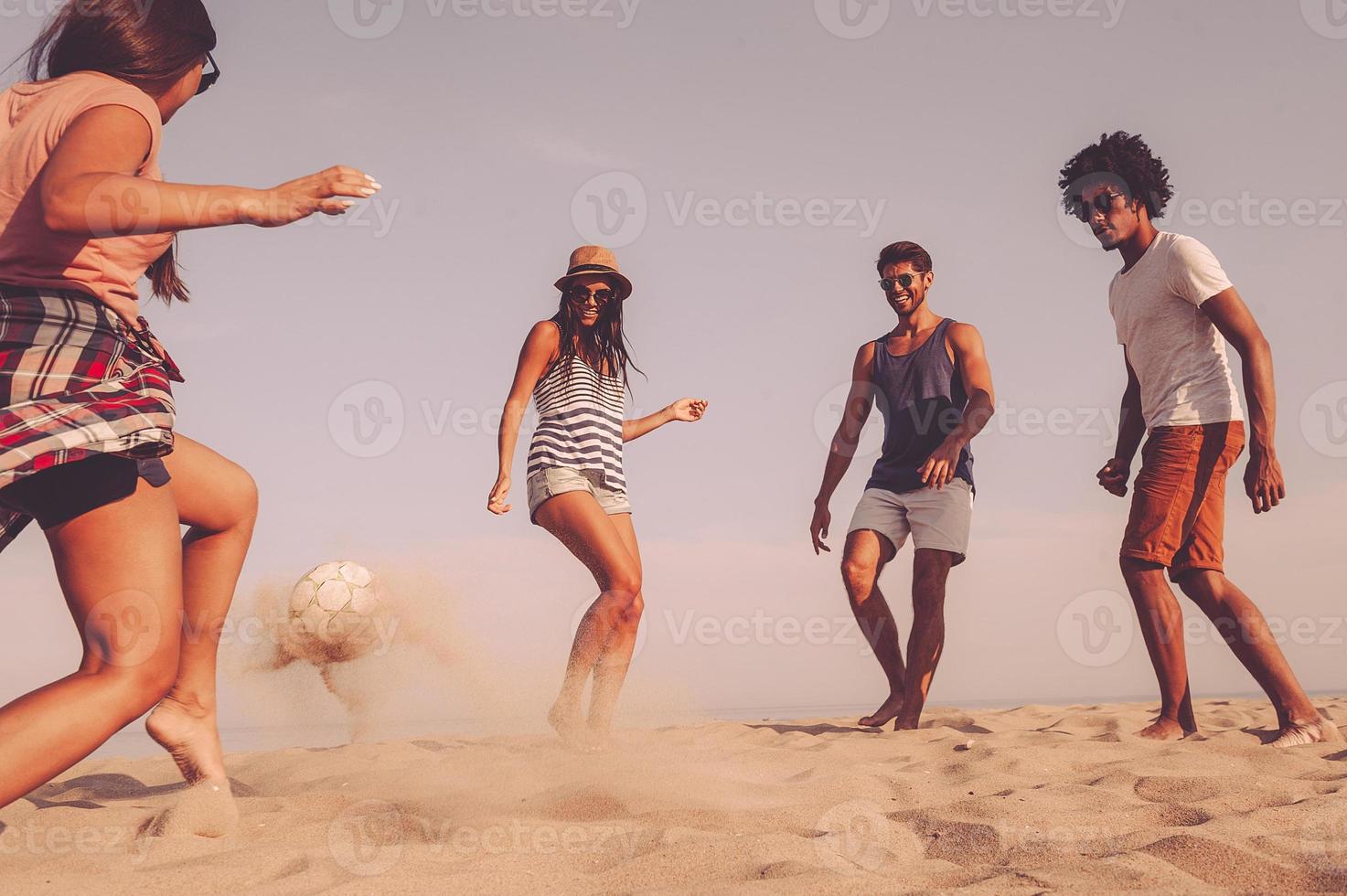 She is really good in soccer. Group of cheerful young people playing with soccer ball on the beach photo