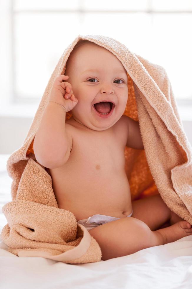 Feeling fresh and happy. Happy little baby smiling at camera while covered with towel photo