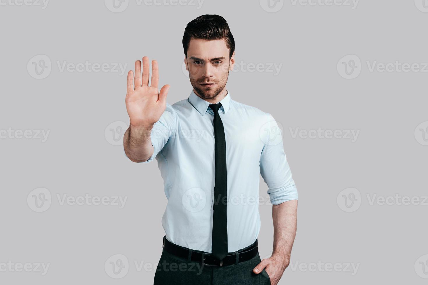 No way to cheat him Serious young man in white shirt and tie gesturing and looking at camera while standing against grey background photo