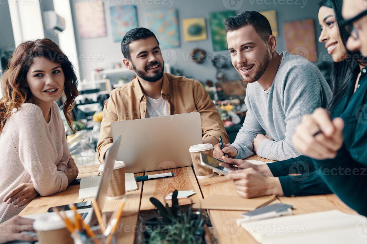 Collaboration. Group of young modern people in smart casual wear discussing something and smiling while working in the creative office photo