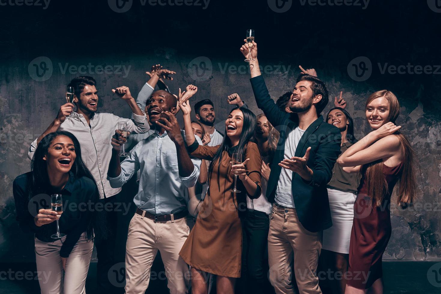 disfrutando de una fiesta increíble. grupo de hermosos jóvenes bailando con flautas de champán y luciendo felices foto