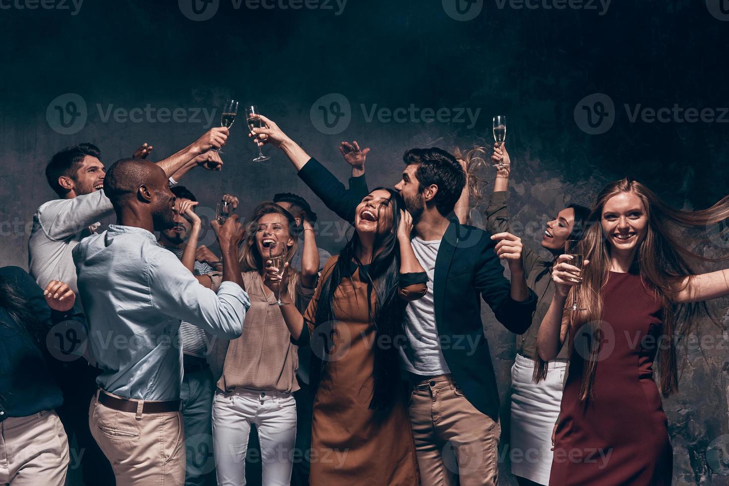 Enjoying amazing party. Group of beautiful young people dancing with champagne flutes and looking happy photo