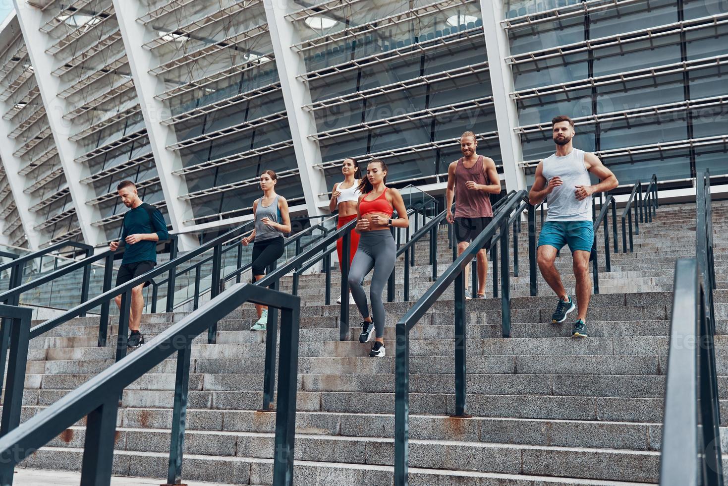 Group of young people in sports clothing jogging while exercising on the stairs outdoors photo