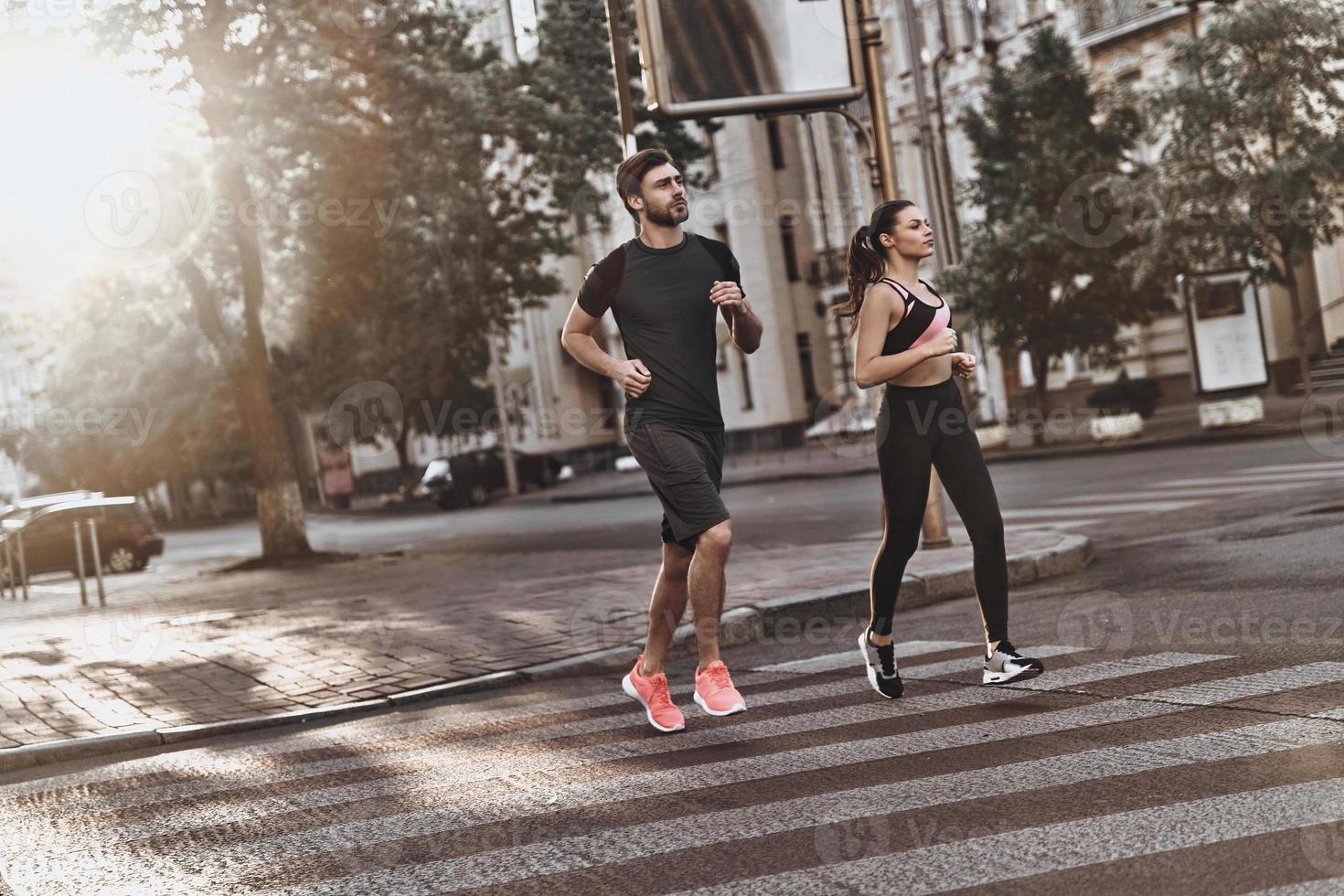 Full of energy. Full length of young couple in sport clothing running through the city street together photo