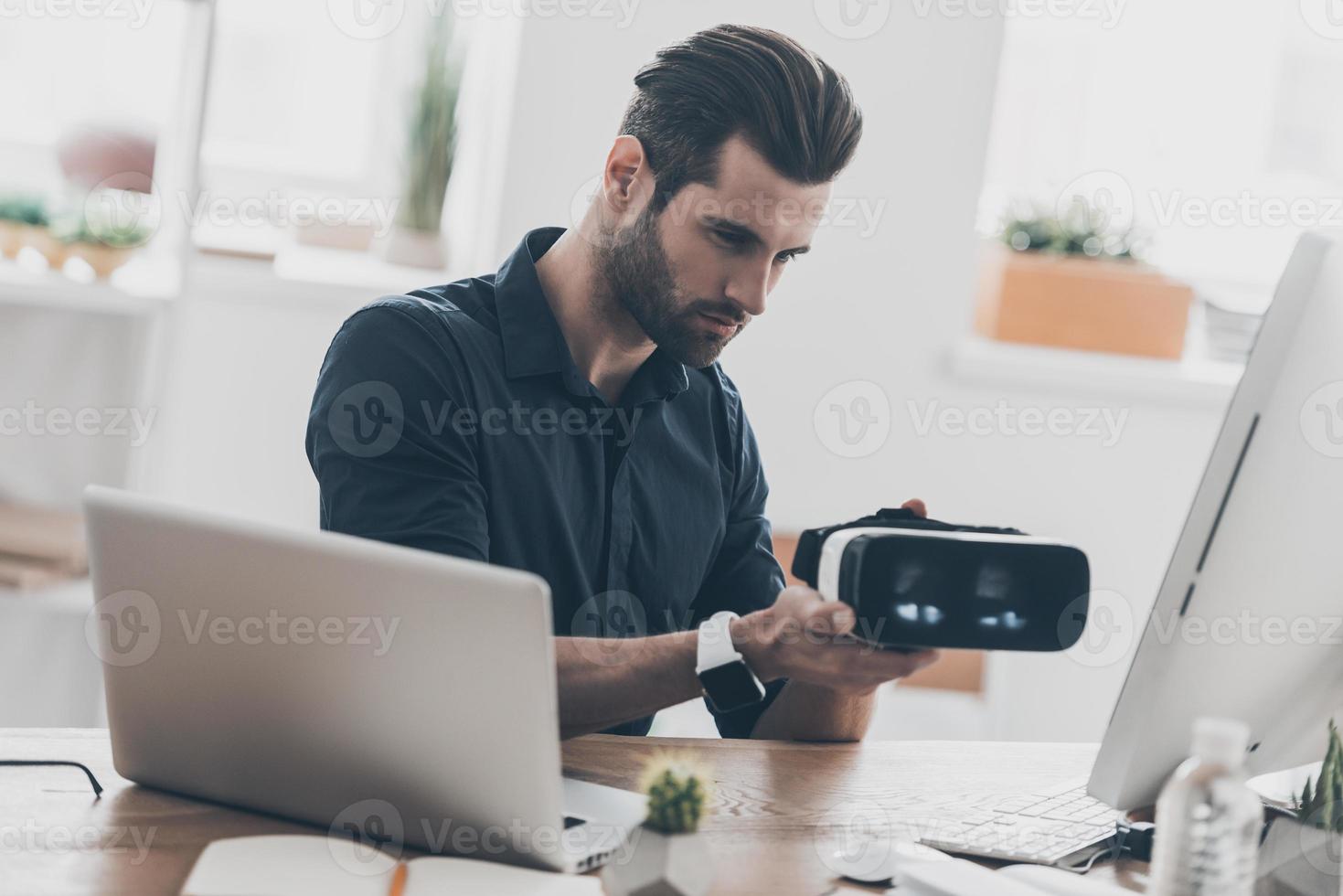 día de trabajo ocupado. apuesto joven revisando el simulador de realidad virtual mientras está sentado en el escritorio en la oficina creativa foto