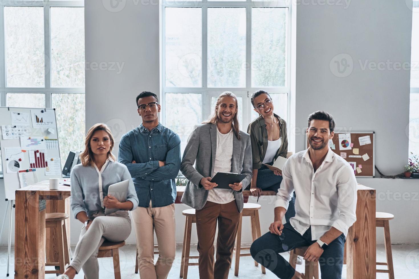 Successful team. Group of young modern people in smart casual wear smiling and looking at camera while standing in the creative office photo