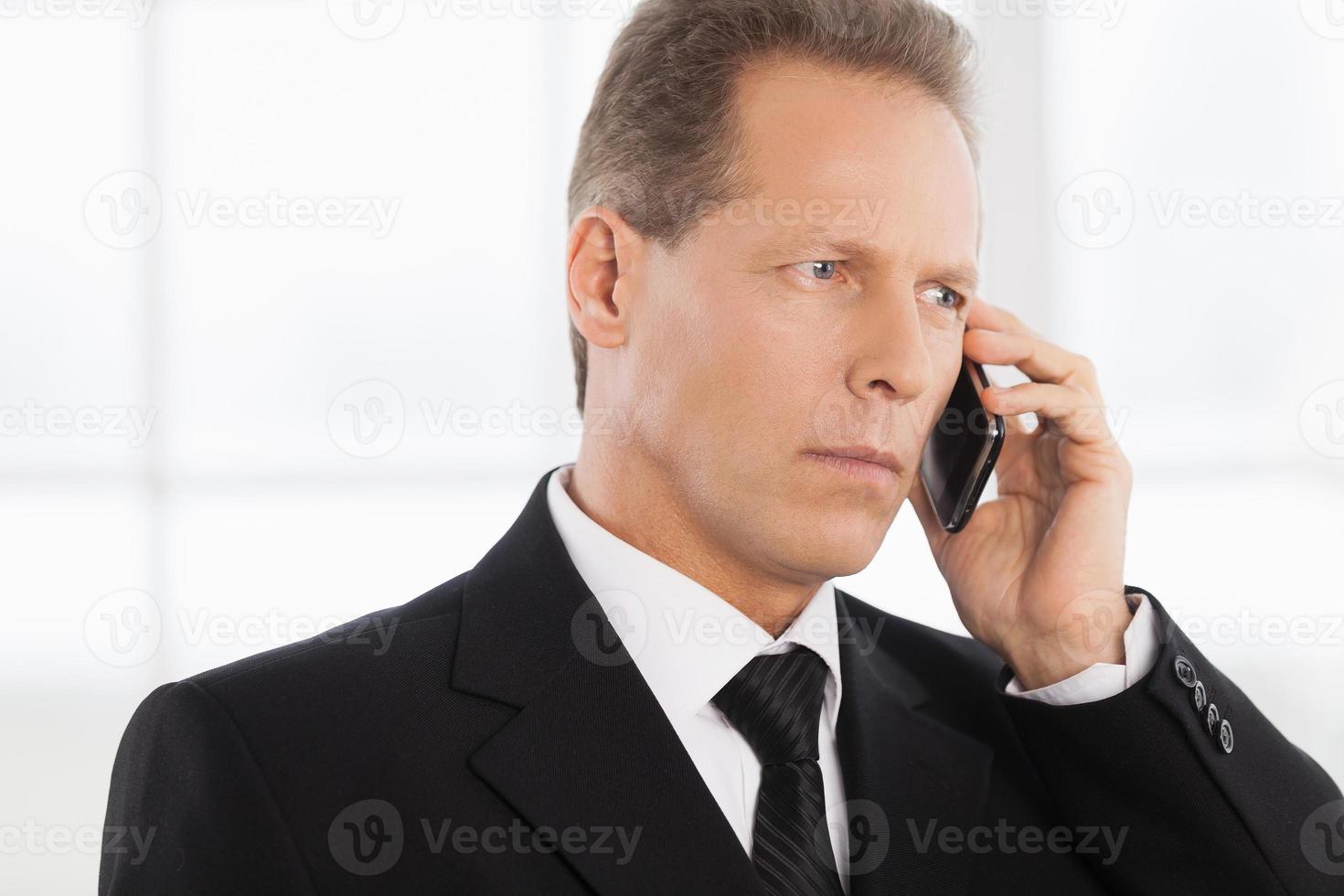 hombre de negocios por teléfono. retrato de un hombre maduro confiado en ropa formal hablando por teléfono mientras está de pie cerca de la ventana foto