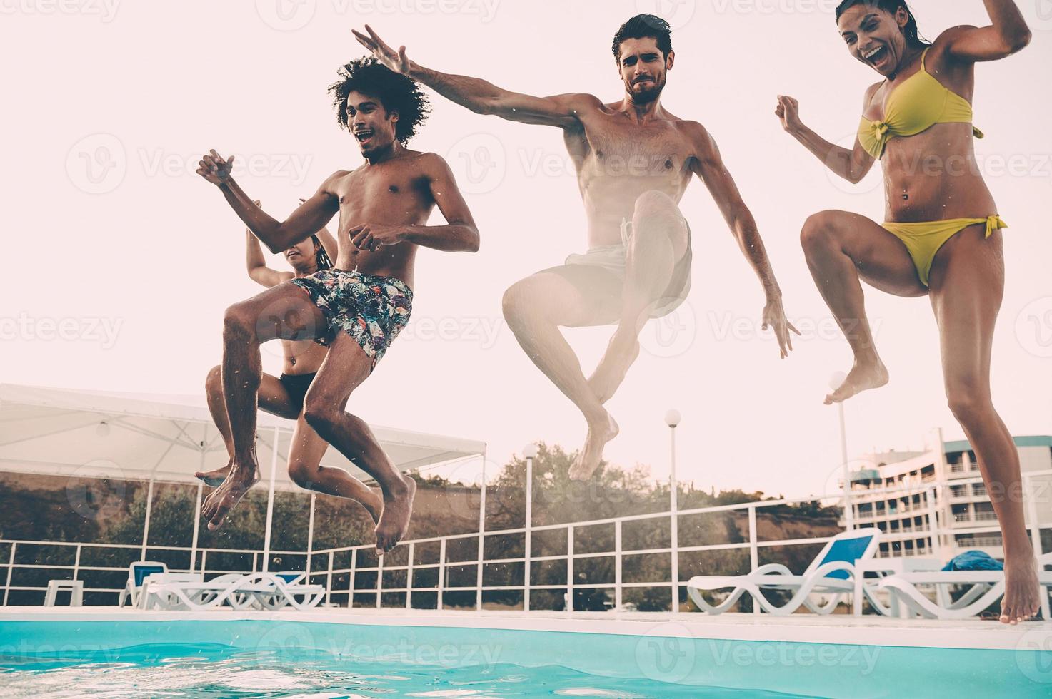 Jumping to the pool. Group of beautiful young people looking happy while jumping into the swimming pool together photo