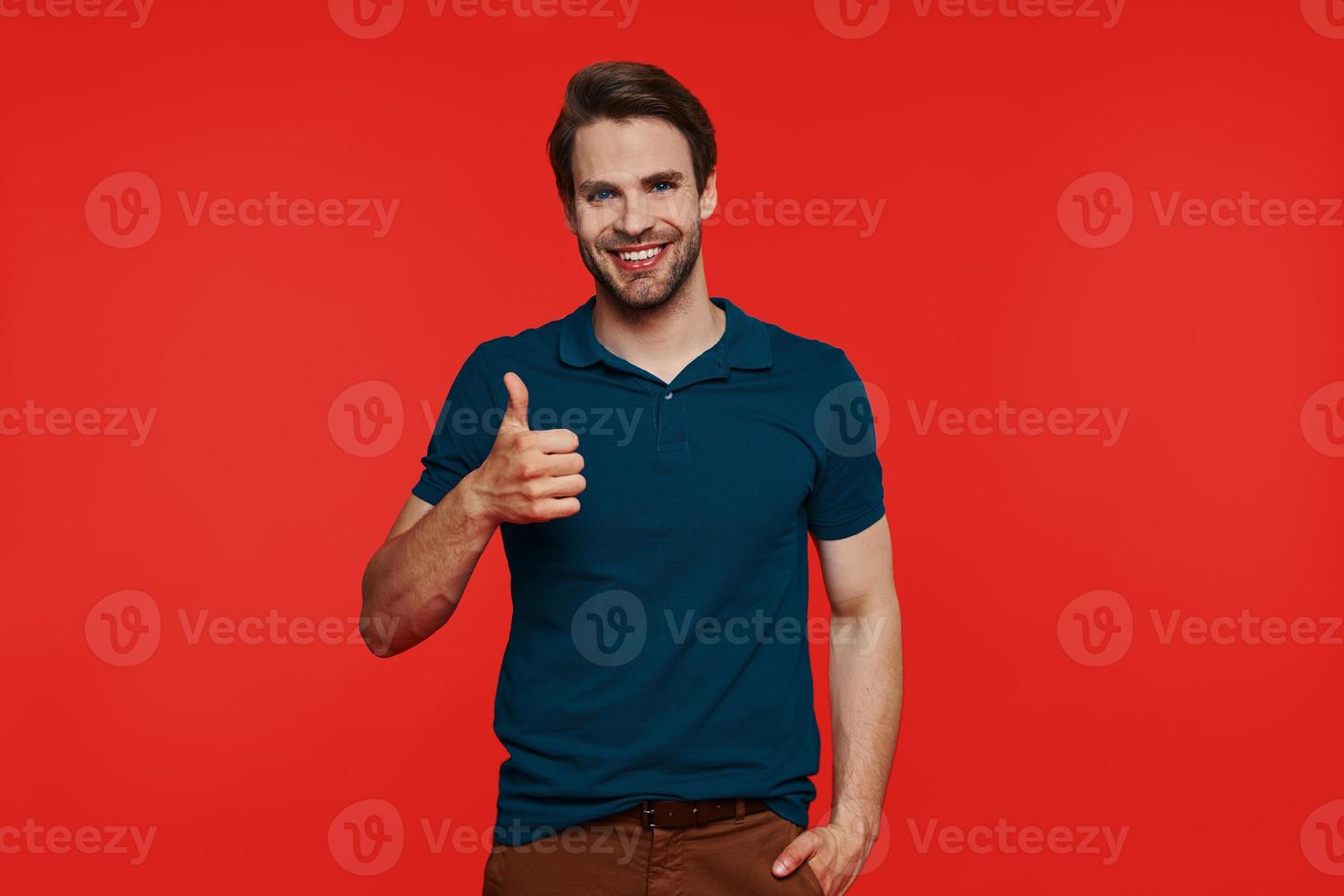 Happy young man in casual wear looking at camera and showing his thumb up photo