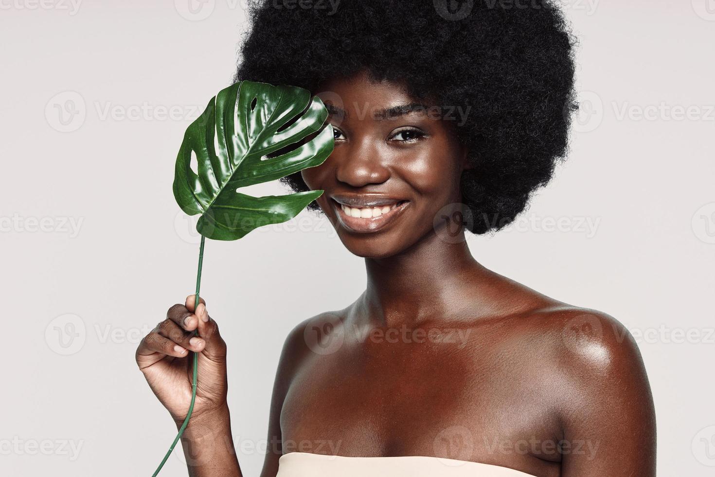 retrato de una hermosa joven africana sosteniendo una planta cerca de la cara y sonriendo foto