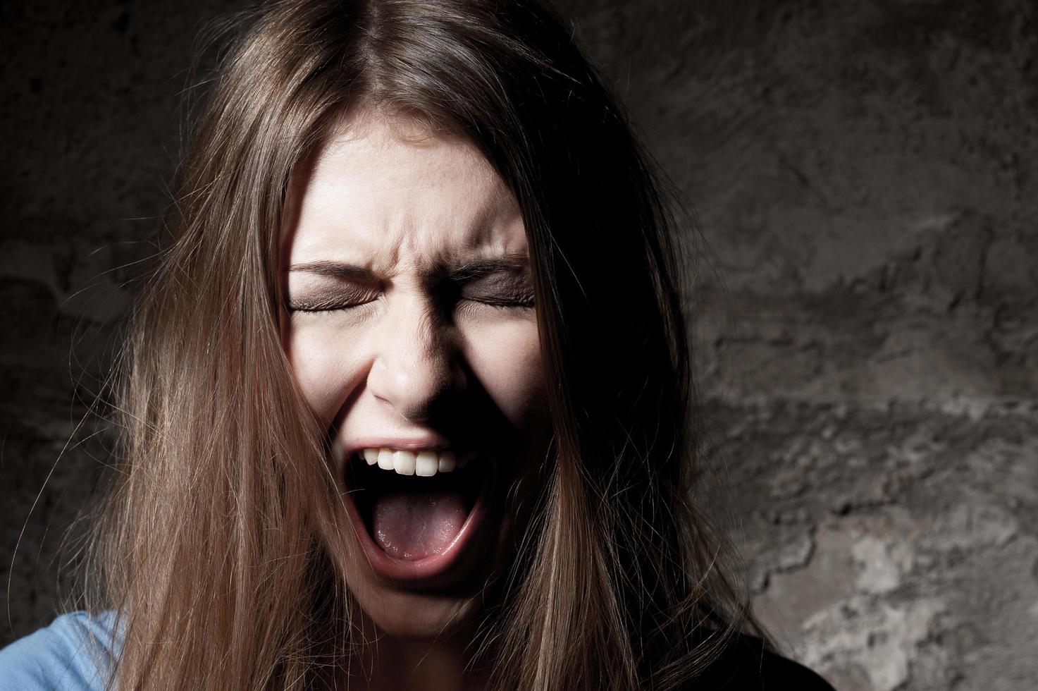 Terrified woman. Terrified young woman keeping eyes closed and shouting while standing against dark background photo