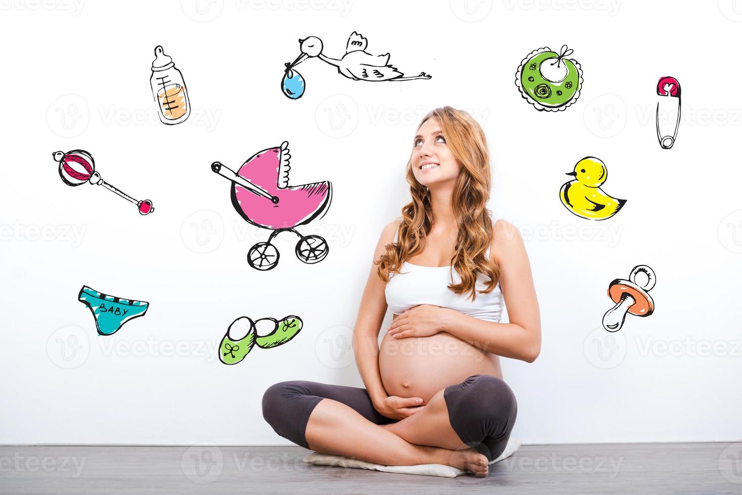 Waiting for a baby. Smiling pregnant woman touching her belly and looking up while sitting against white background photo