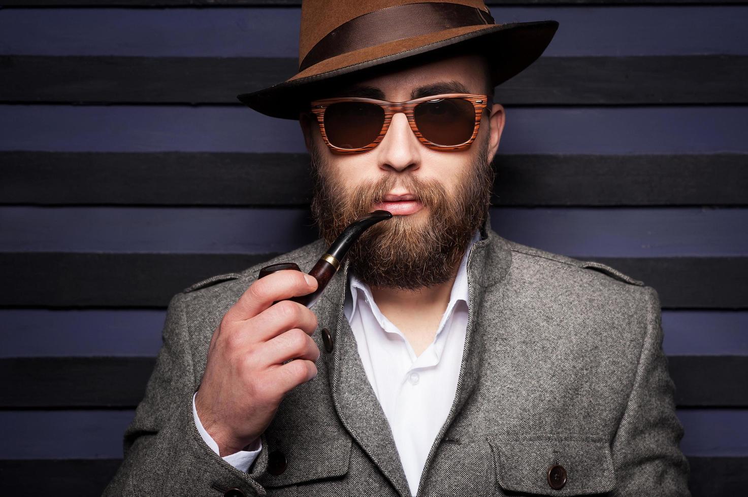 fumando una pipa. retrato de un apuesto joven con sombrero fumando una pipa y mirando a la cámara foto